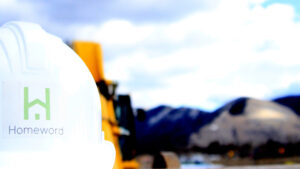 Homeword hardhat in front of backhoe and Mt. Sentinel