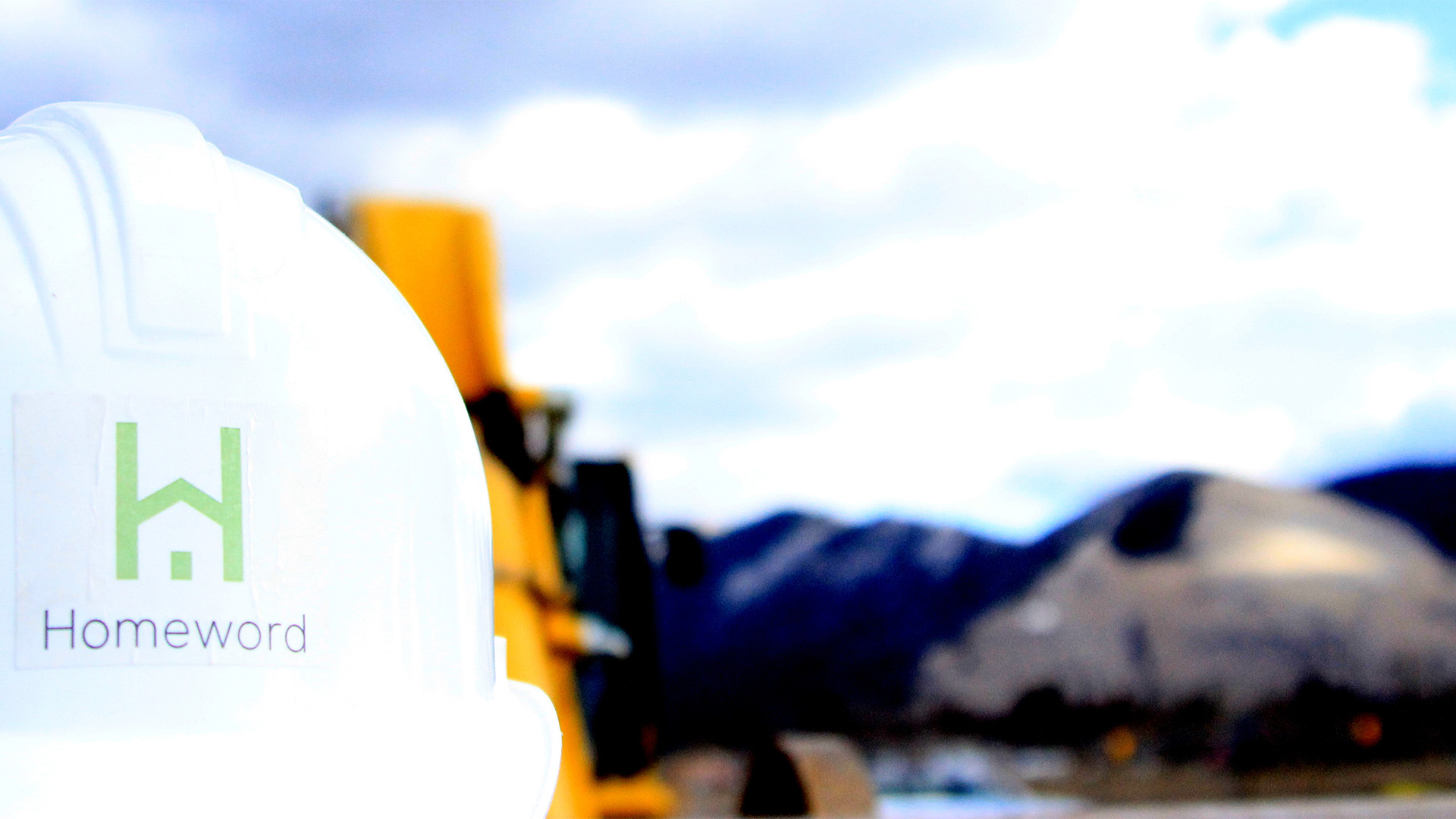 Homeword hardhat in front of backhoe and Mt. Sentinel