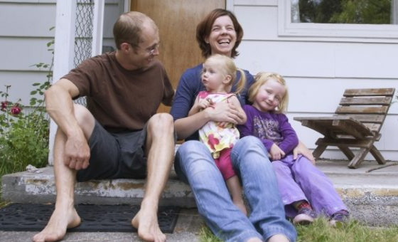 Family sitting on front step of their new home