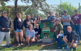 Group of UM students around little free library and pantry
